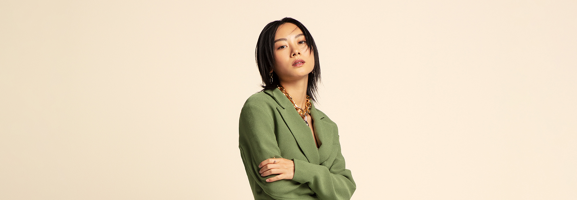 A woman in a green blazer and statement necklace striking a pose