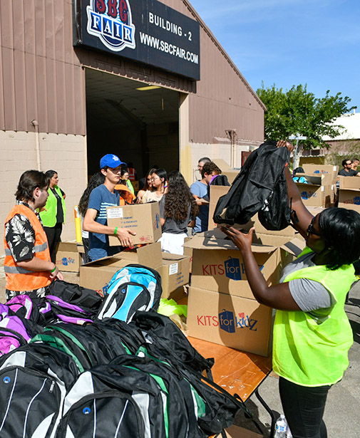 Backpacks on a table with volunteers putting backpacks in boxes