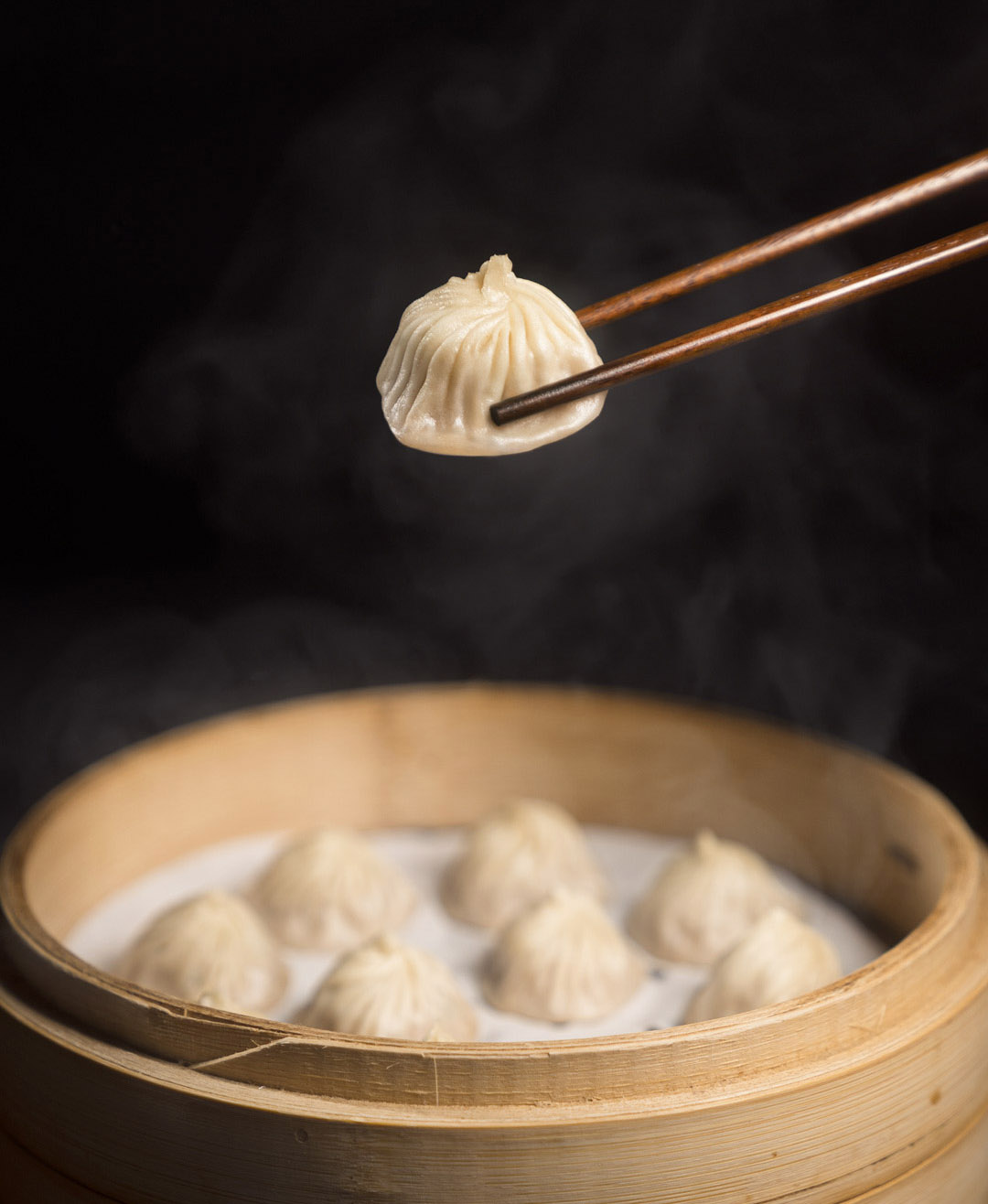 Dumplings in bowl with dumpling on chopsticks