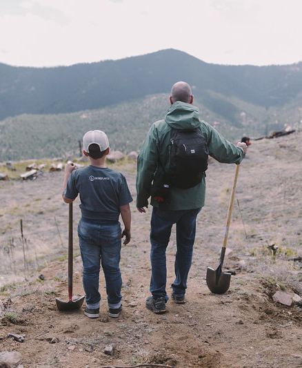 Two people holding shovels while looking toward mountain