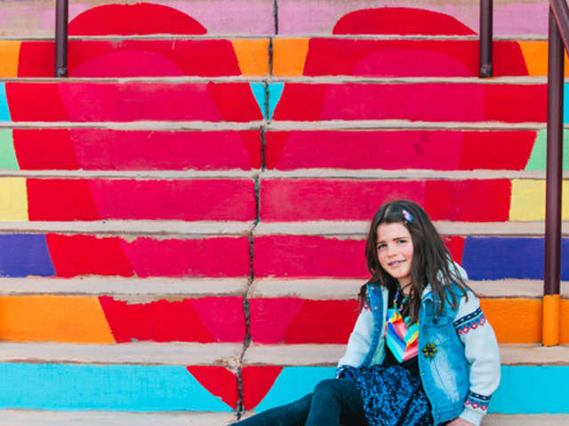 A middle school age girl sitting in front of a stairway painted with a heart