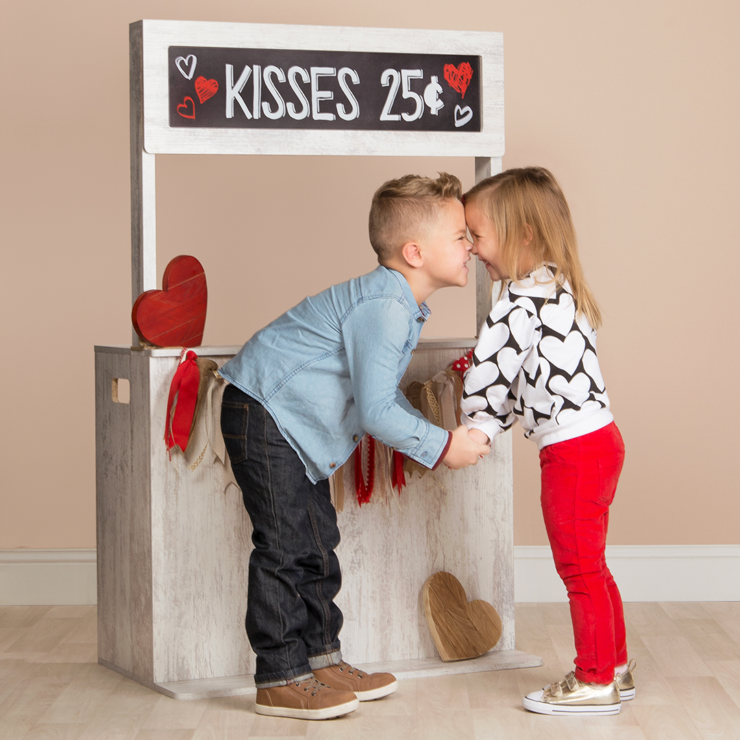 A girl and boy posing in front of a Valentine's Day photoshoot prop booth.