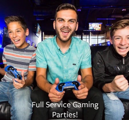 Boy with grey and pink striped shirt and blue jeans, guy with green shirt and boy with black shirt and blue jeans playing video games.
