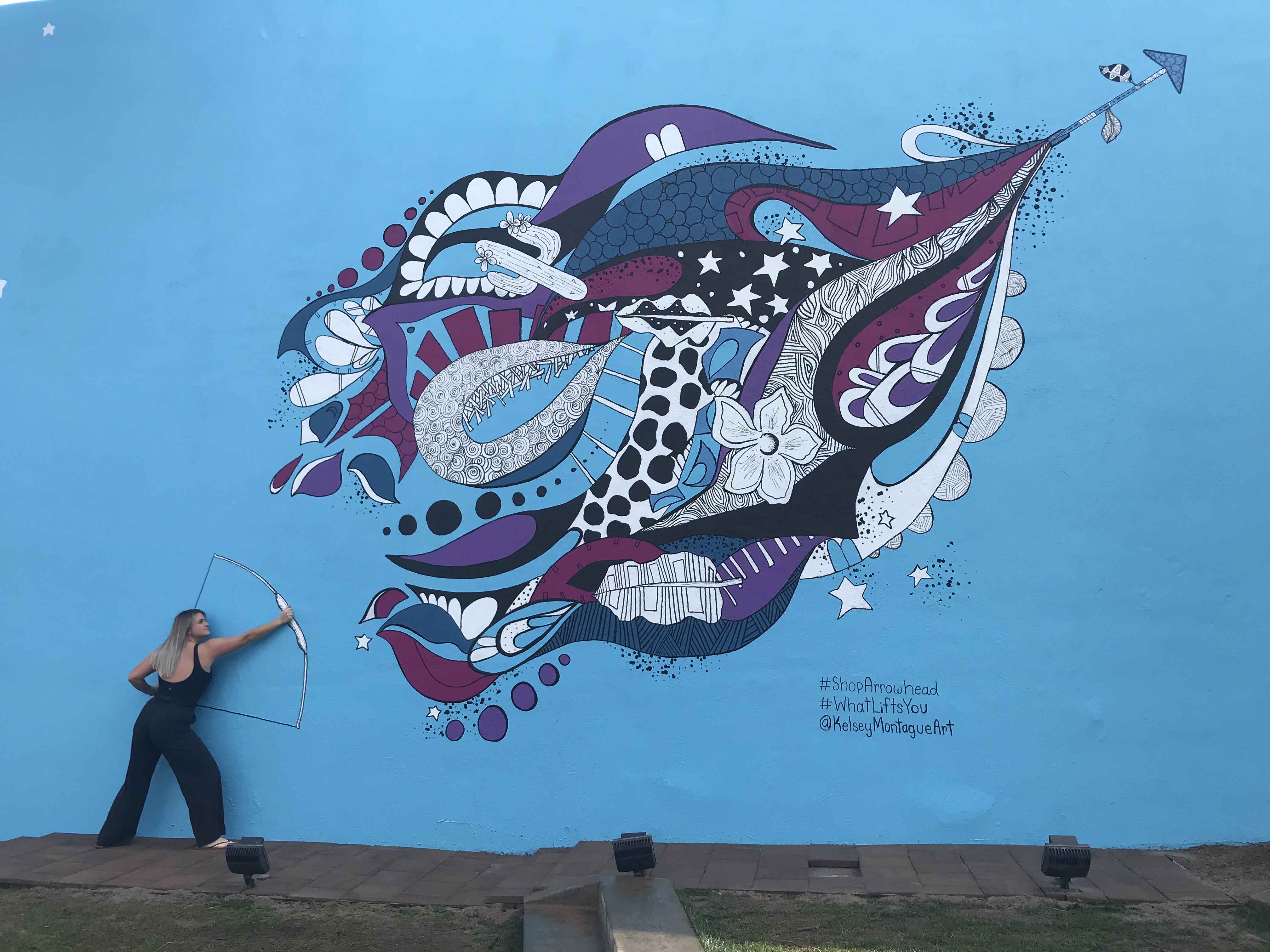 female posing with bow and arrow in front of art work