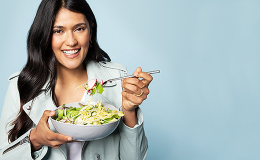 girl with black hair eating salad from a white bowl