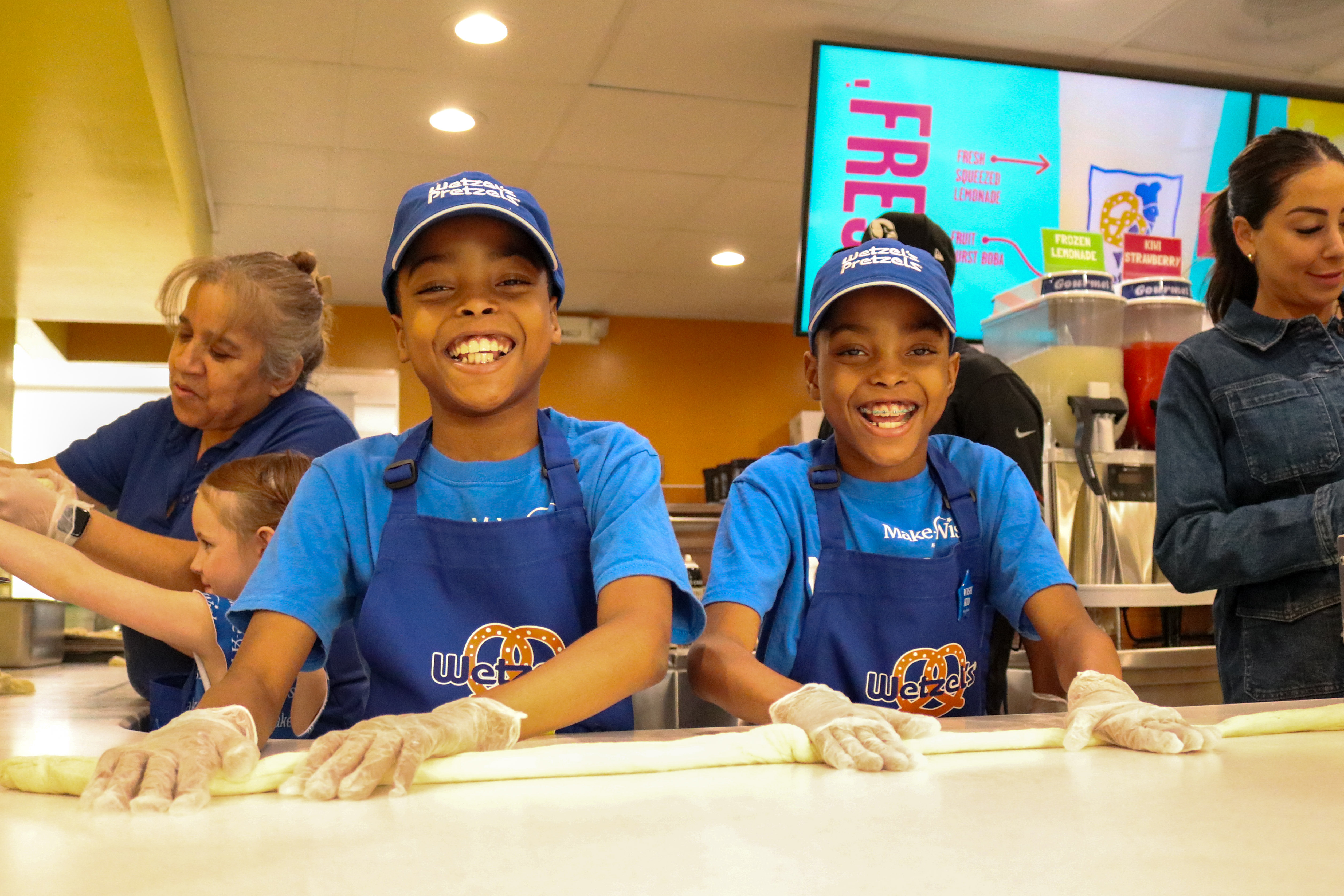 kids and adults smiling rolling pretzel dough on the counter 
