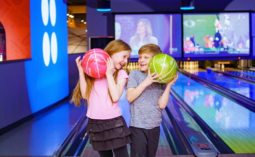 a young girl and boy holding colorful bowling balls in a bowling alley.