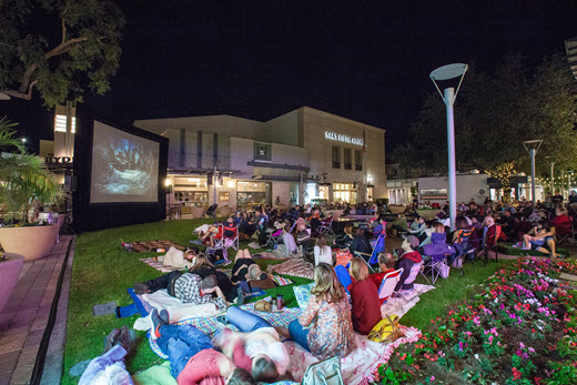 People watching a movie , seated in the grass.