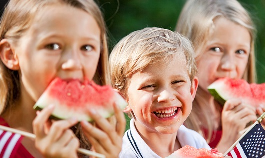 Three children - 2 girls and 1 boy - eating watermelon.