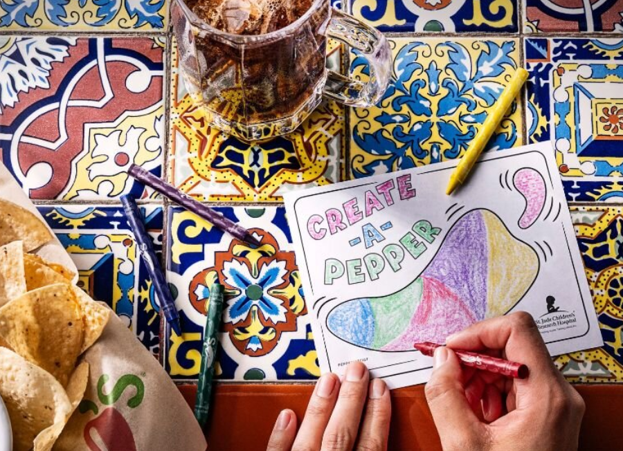 A person at Chili's restaurant coloring a piece of paper that says Create-A-Pepper with chips and soda on the table. 
