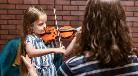 little girl playing the violin as teacher instructs 