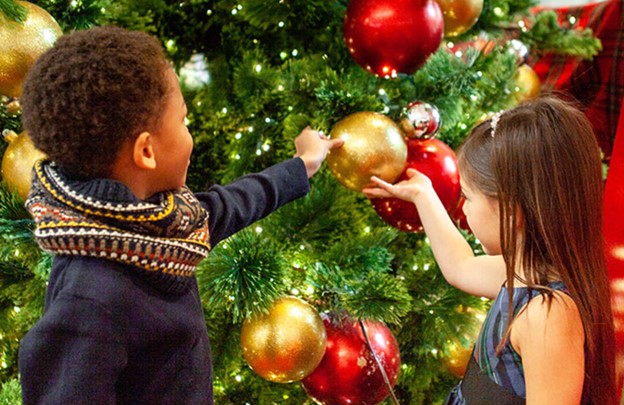 a little boy and little girl playing with ornaments on a Christmas tree