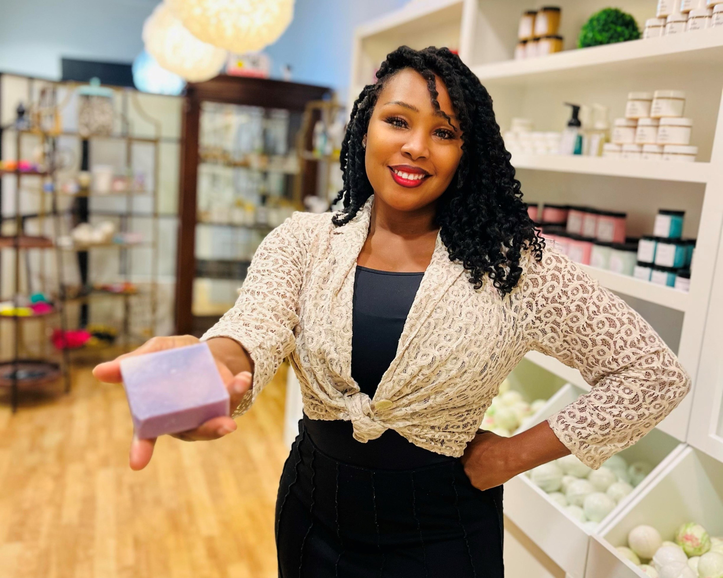 Women in black dress and white top tied at waist, holding a bar of lavender soap in a retail store. 