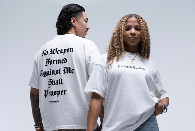 Two people wearing t-shirts. The back of the shirt says "No weapon formed against me shall prosper" and the front of the shirt says "powered by God". 