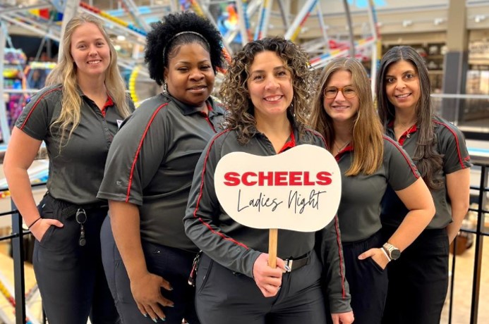 Five female Scheels employees smiling at camera with one holding a sign that says SCHEELS Ladies Night