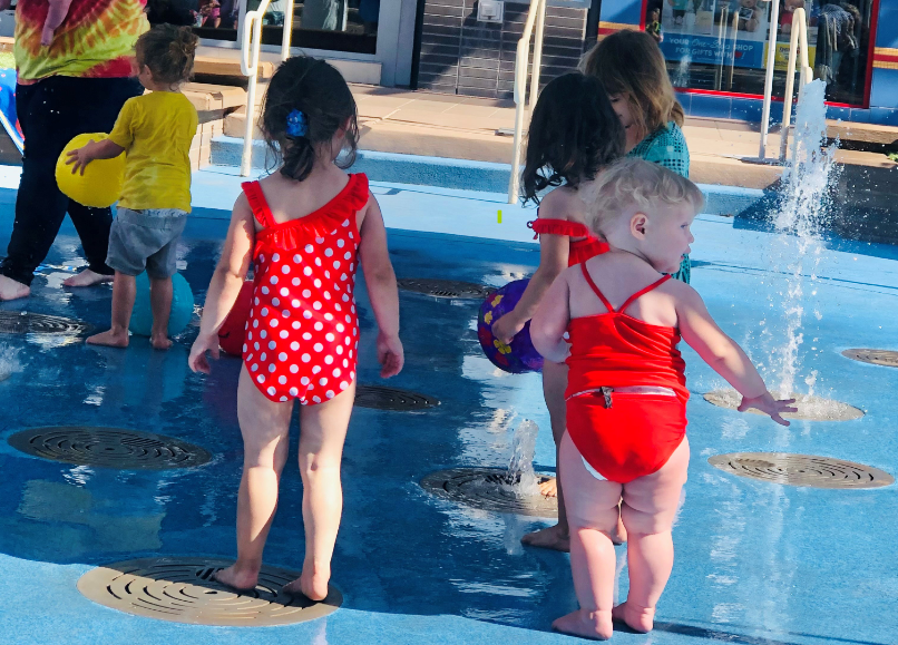 Toddlers dressed in swim suits playing at a splash pad 