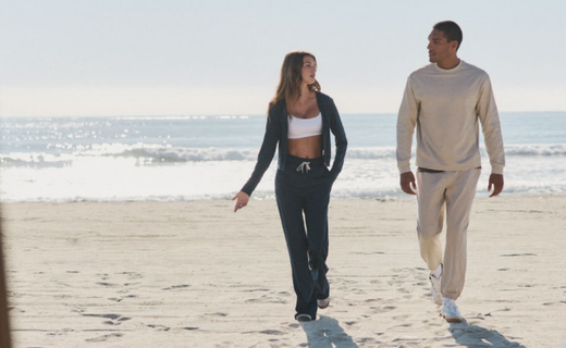 a man and a woman walking on the beach in sweat suits 