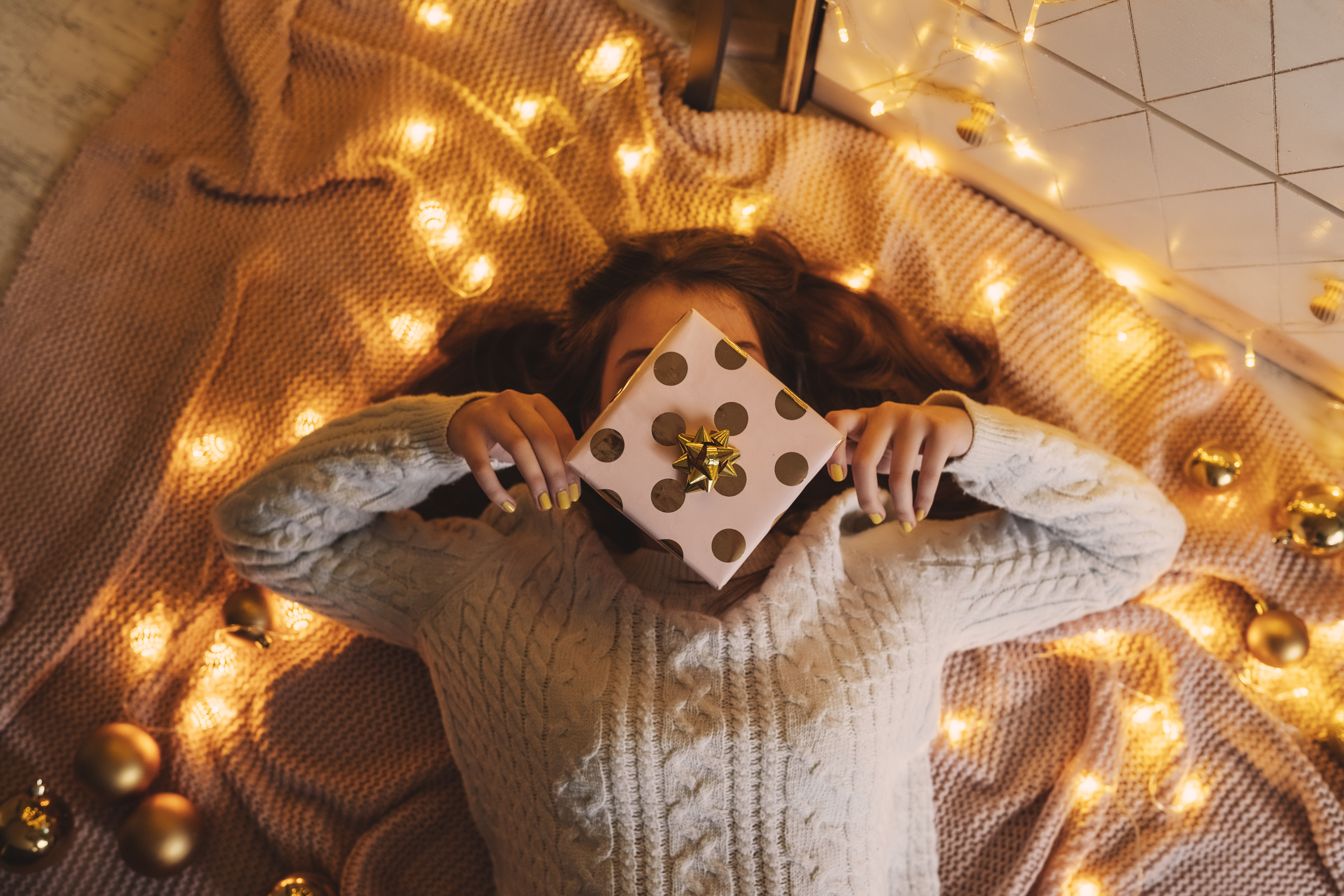 Picture of girl laying on floor holding gift wrapped present over her face.