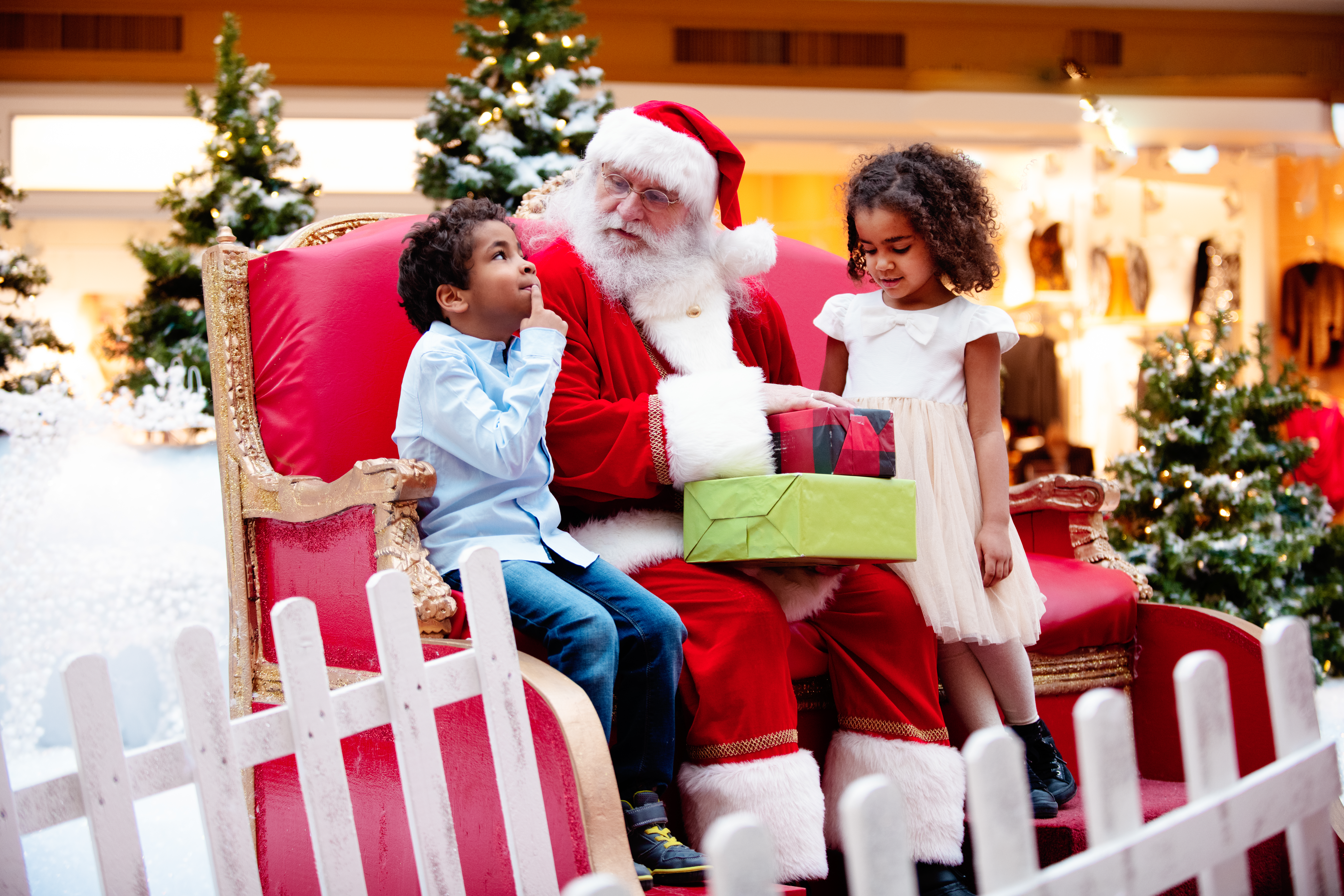 Santa sitting and holding 2 gifts with a young boy and girl