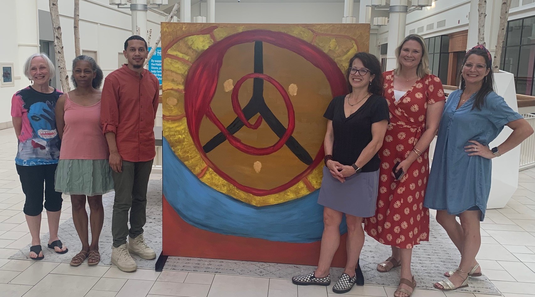 Piece of art with circular design and brown blue yellow red and black colors, with 6 people standing around it