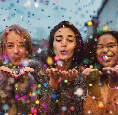 photo of 3 women blowing confetti towards the camera 