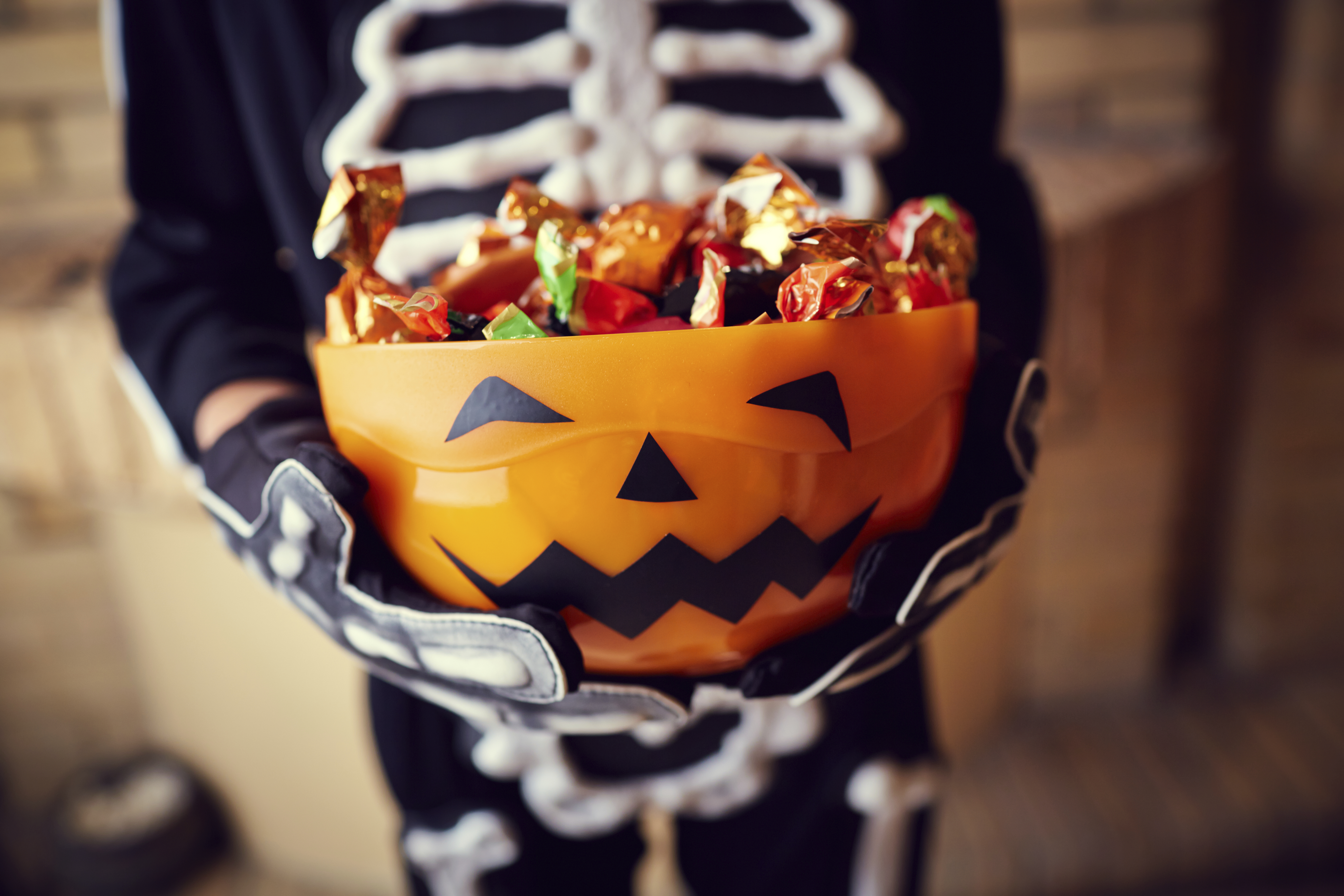 kid in a skeleton costume holding a pumpkin bowl filled with candy