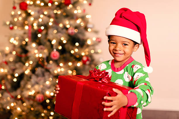 little boy wearing pajamas and a Santa hat holding a red gift