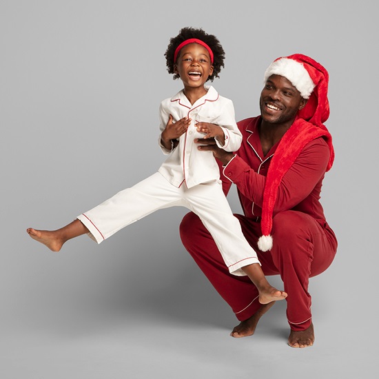 Father holding up daughter both wearing holiday pajamas