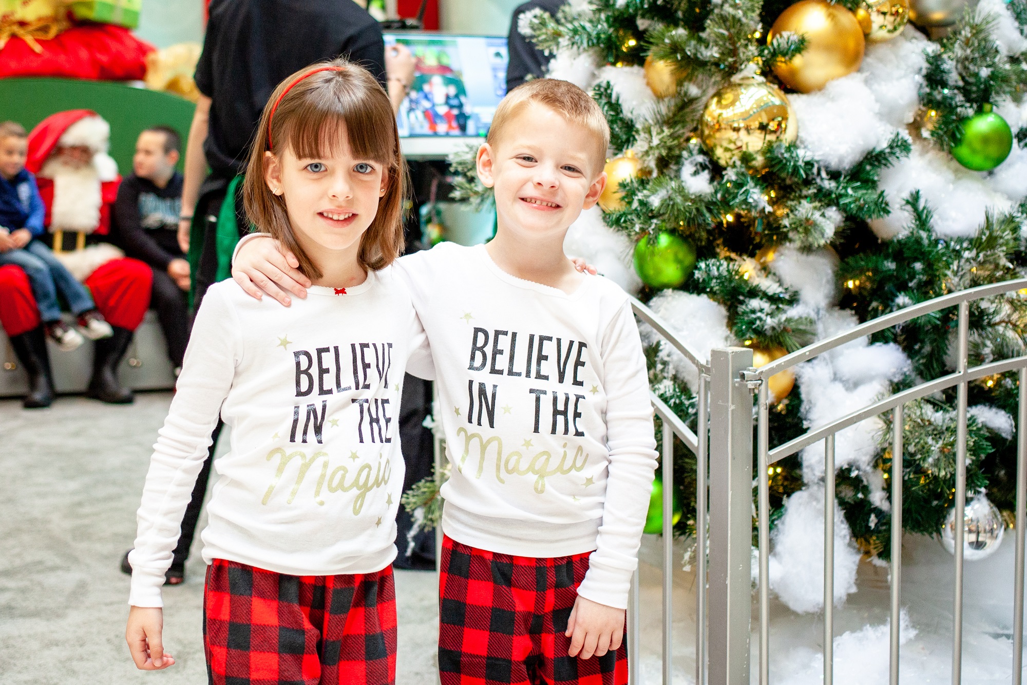 Kids wearing holiday pajamas with Santa in the background