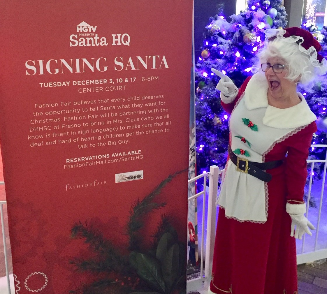 Mrs. Claus pointing at a Signing Santa sign