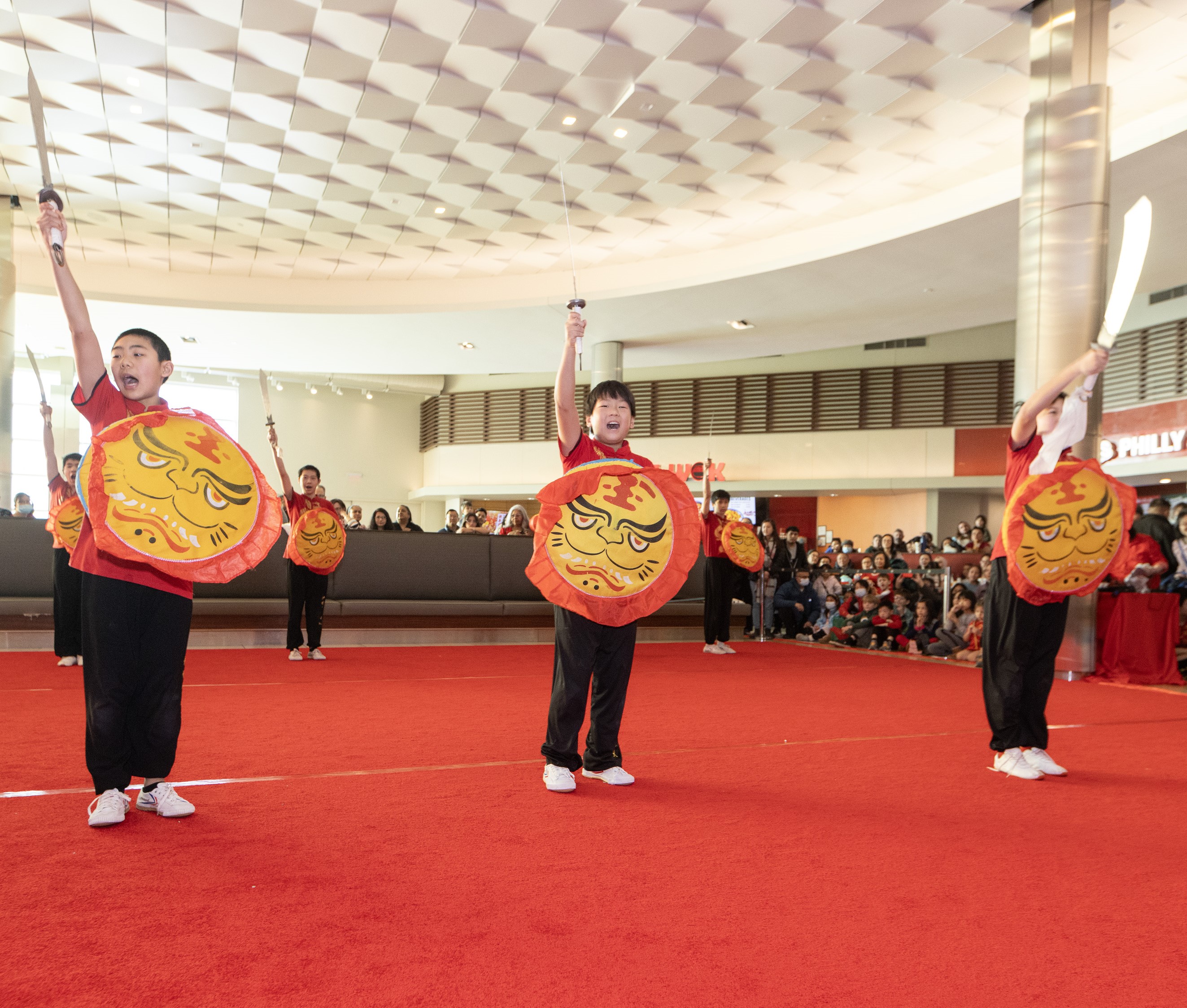 Kung Fu group performing with knives on a red carpet with audience watching around them. 