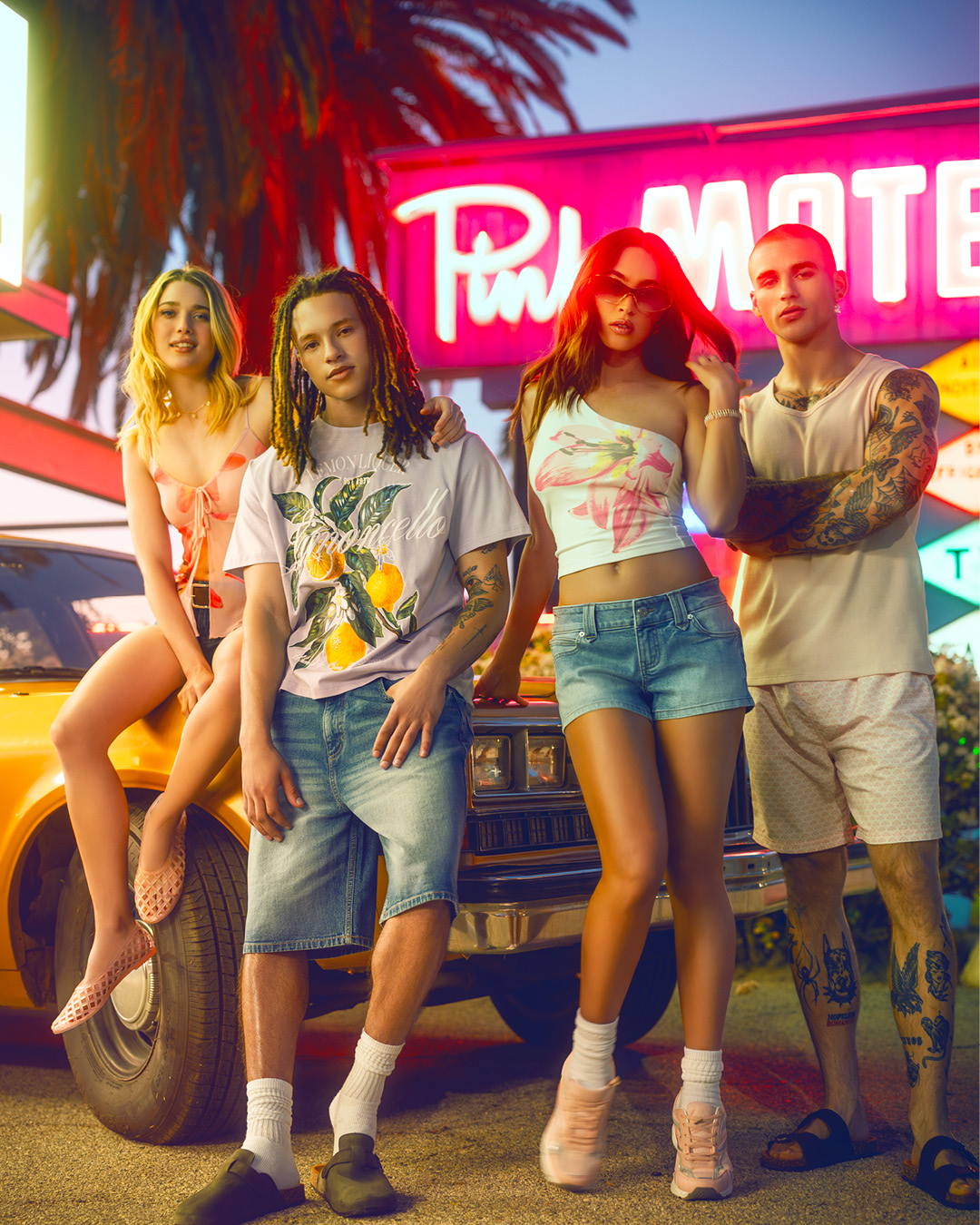 Two male and two female models wearing trendy clothing while leaning on a vehicle