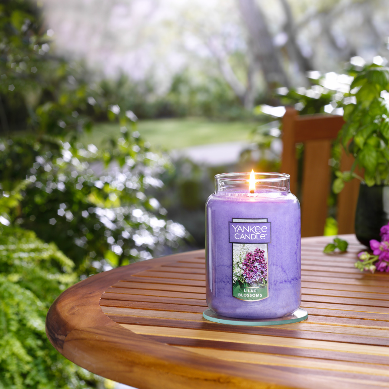 A illuminated Lilac Blossoms jar candle on a wooden table, in the garden