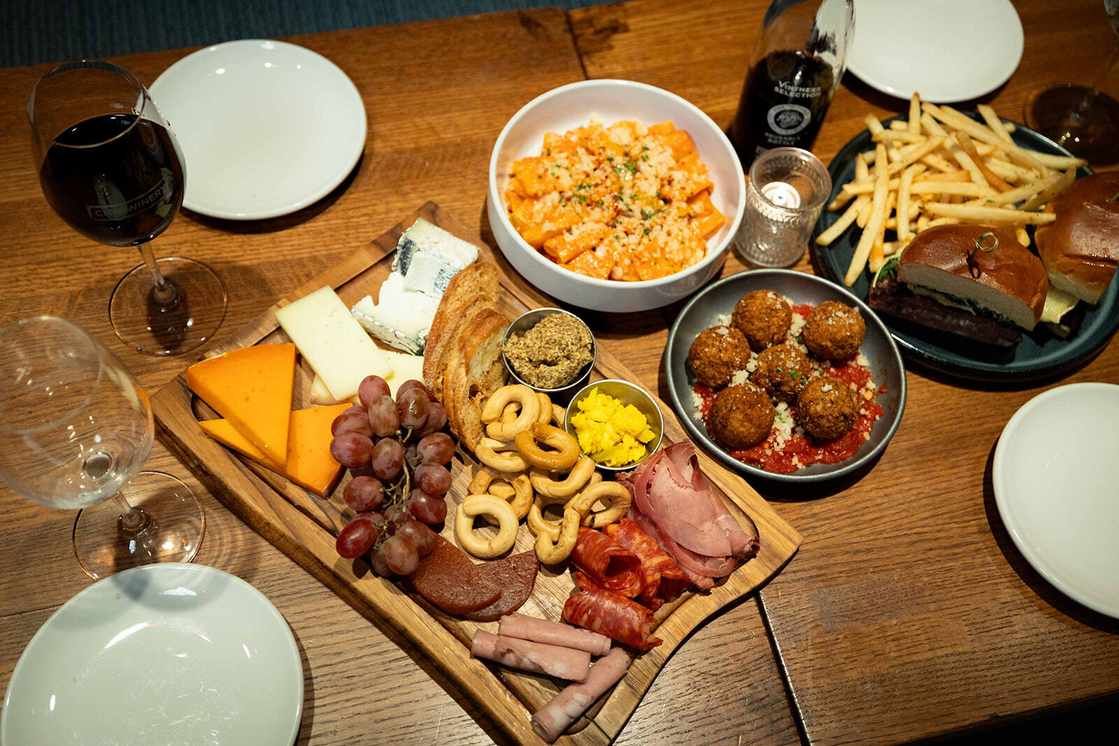 Warm-toned photo of hands clinking a City Winery wine glass and citrus cocktails with salted rims over a table of shared appetizers