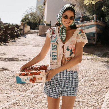 Woman holding a box of tomatoes walking down a pebbled street.