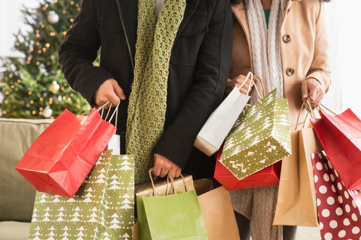 Two people holding many shopping bags in colors green, red and white.