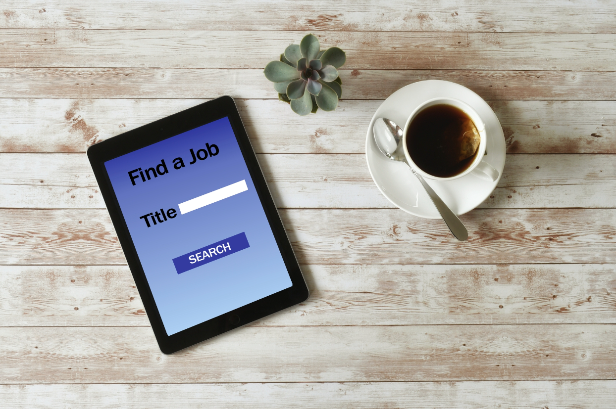 Tablet and coffee mug sitting on top of a table. Tablet copy reads " Find a job. Title. Search"