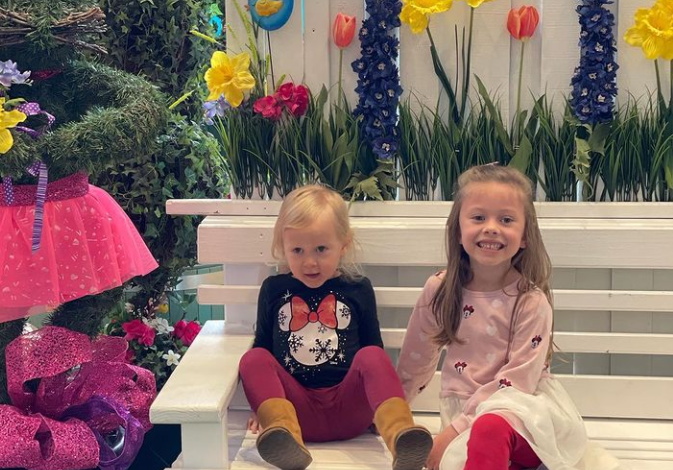 Two little girls sitting on bench with spring decor.