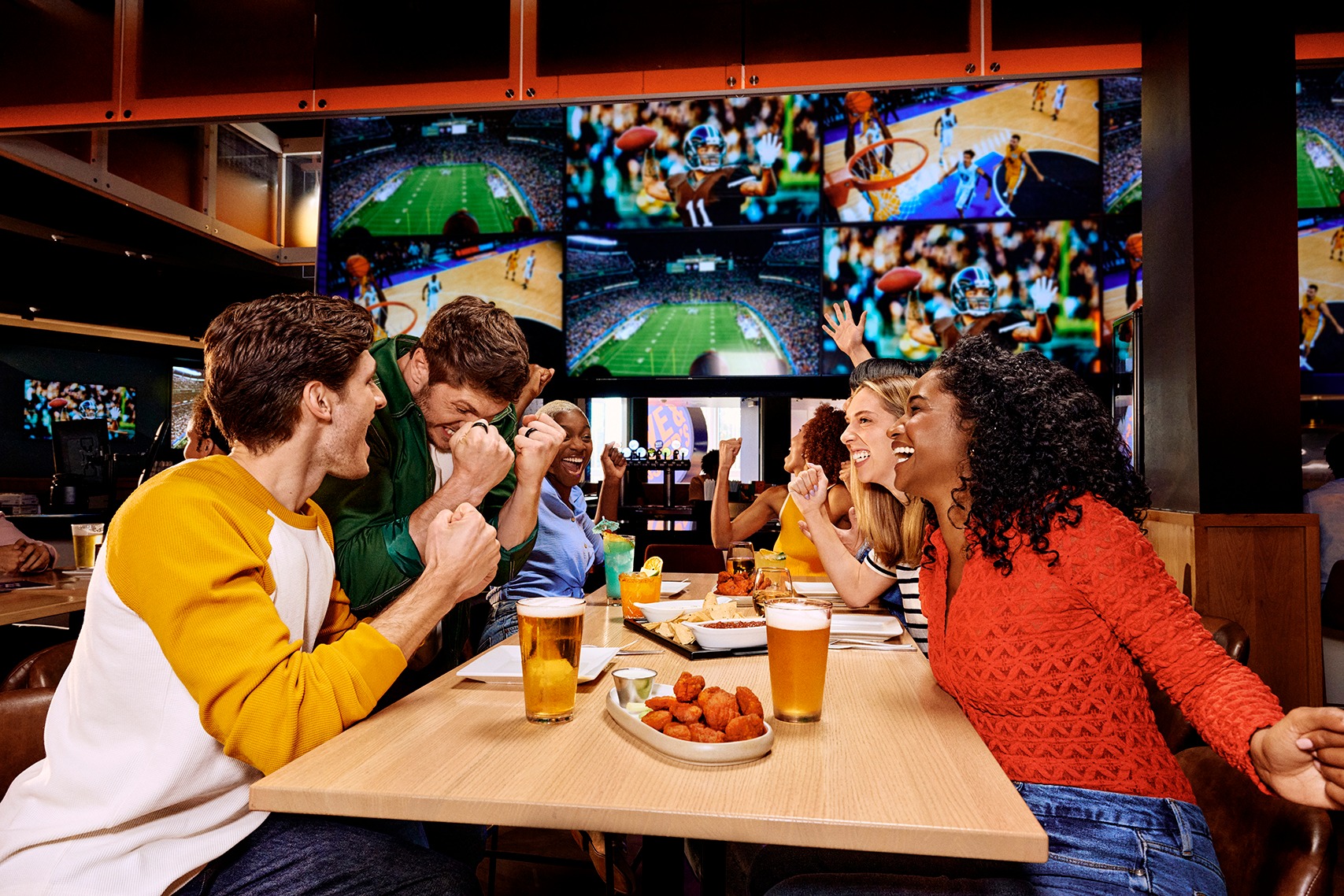 six people sitting at a table eating and cheering for their teams