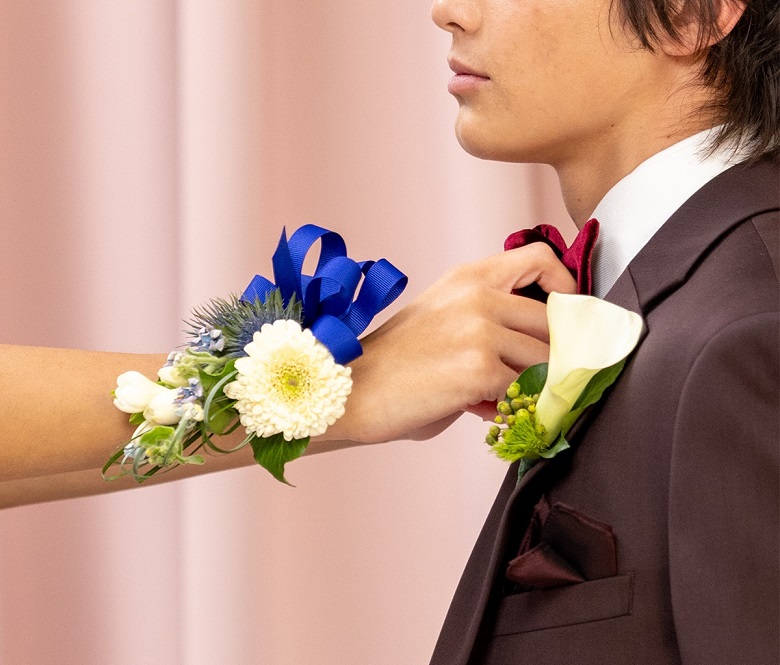 Person with a wrist corsage fixing the bowtie of a man in a tux