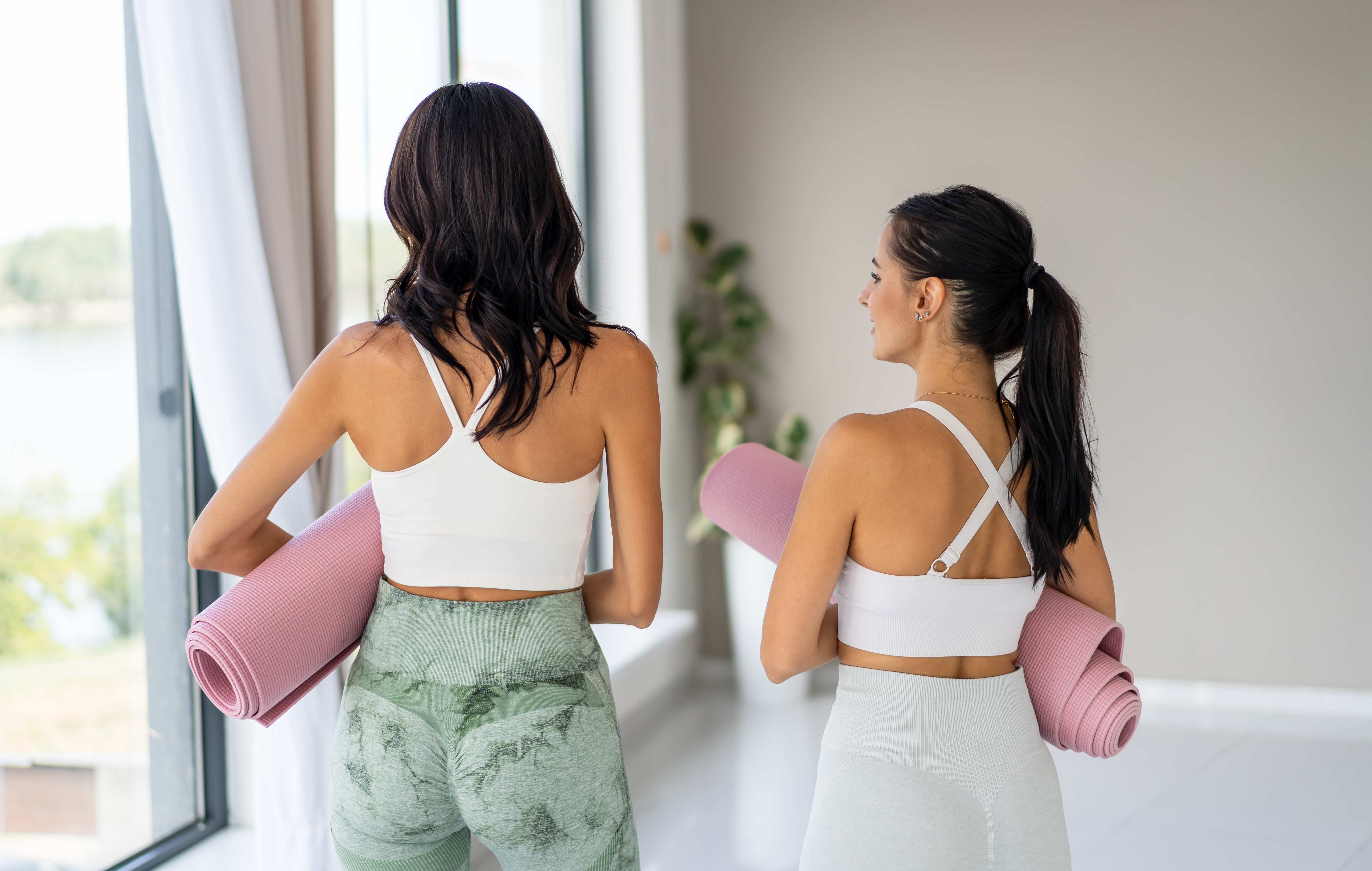 two women wearing athletic gear and carrying pink yoga mats