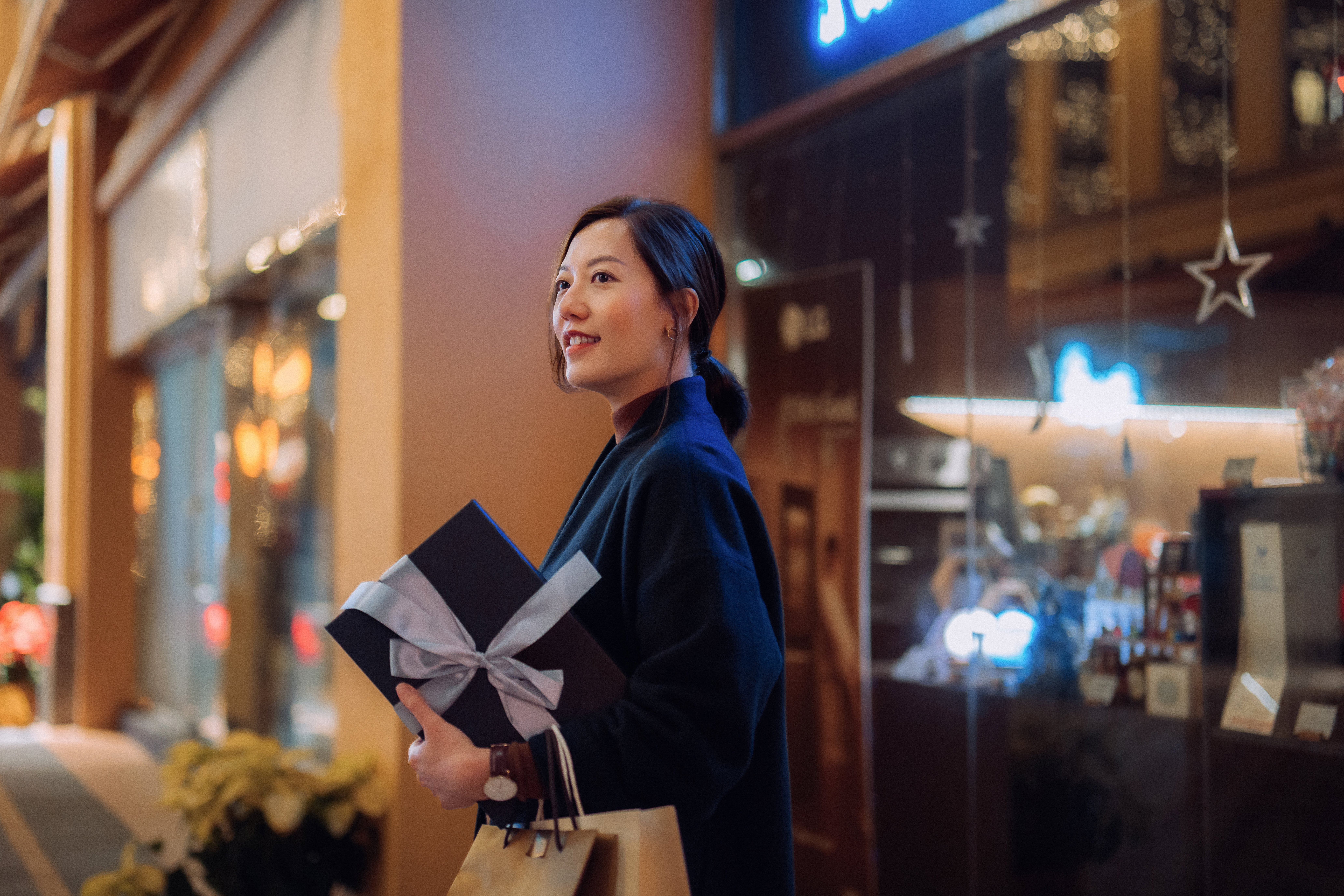 woman in shopping center holding a wrapped gift that has a bow