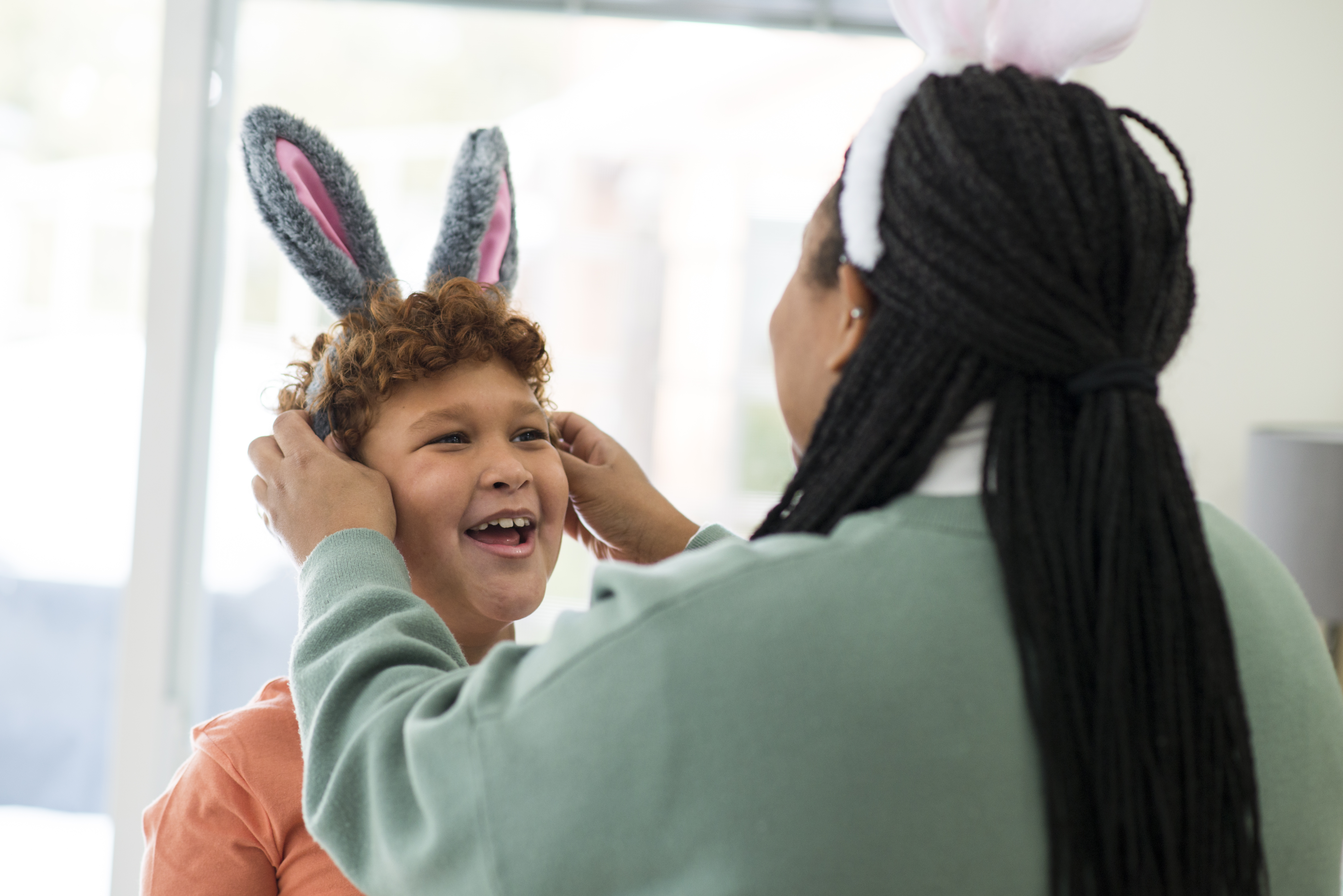 woman placing Easter bunny ears on young boy who is smiling 
