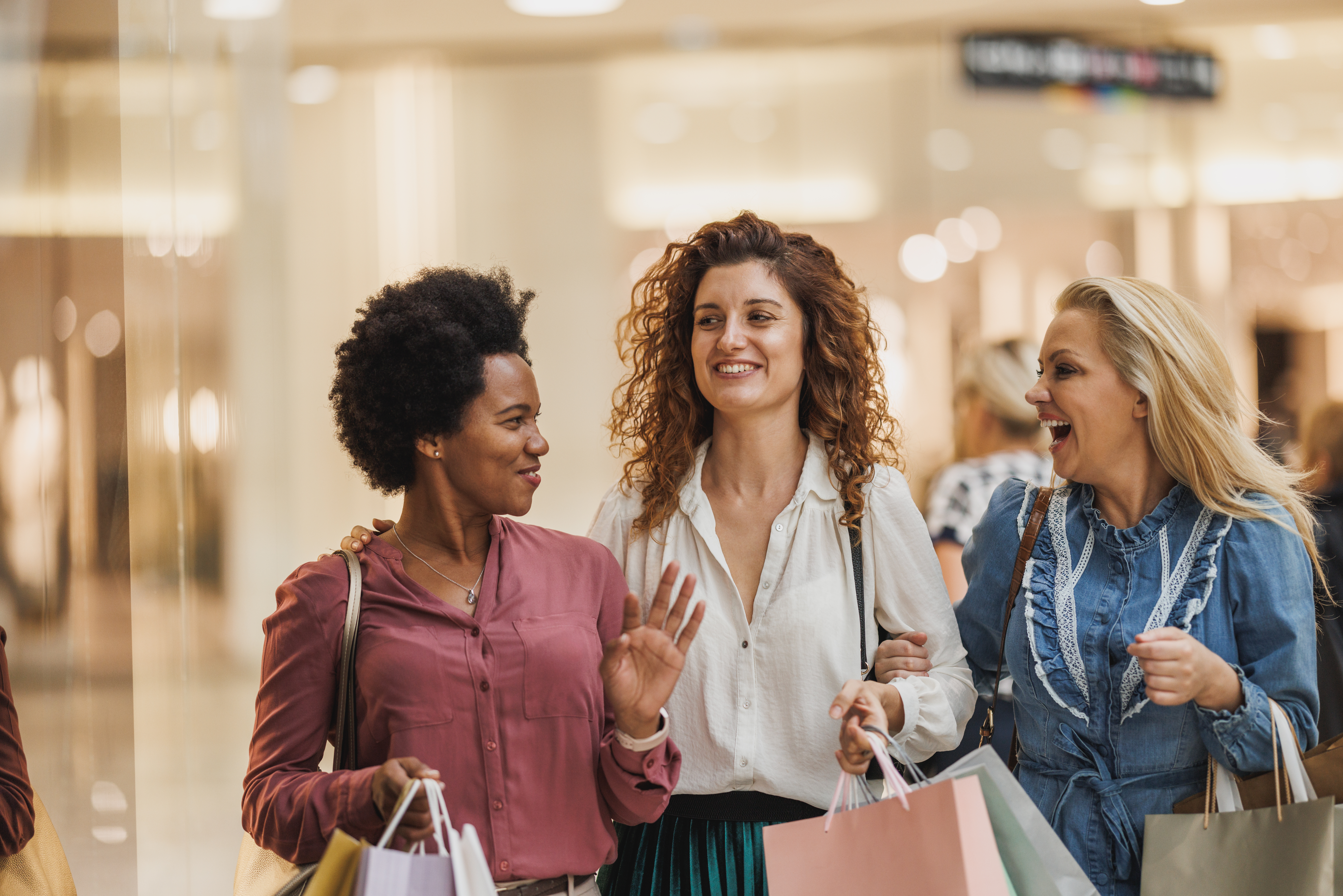 3 women laughing together while shopping and holding shopping bags