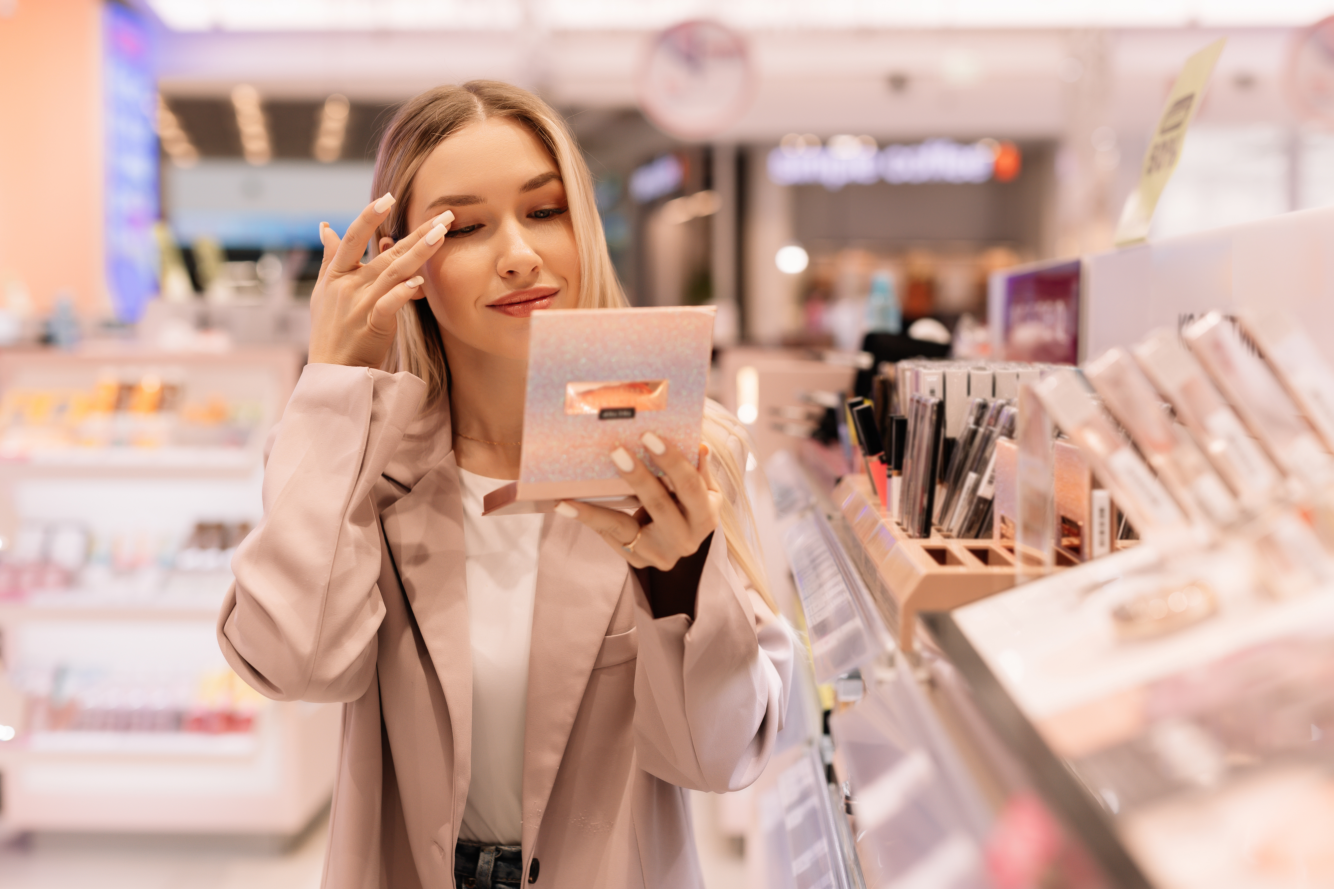 blonde woman in store applying eye makeup using compact mirror