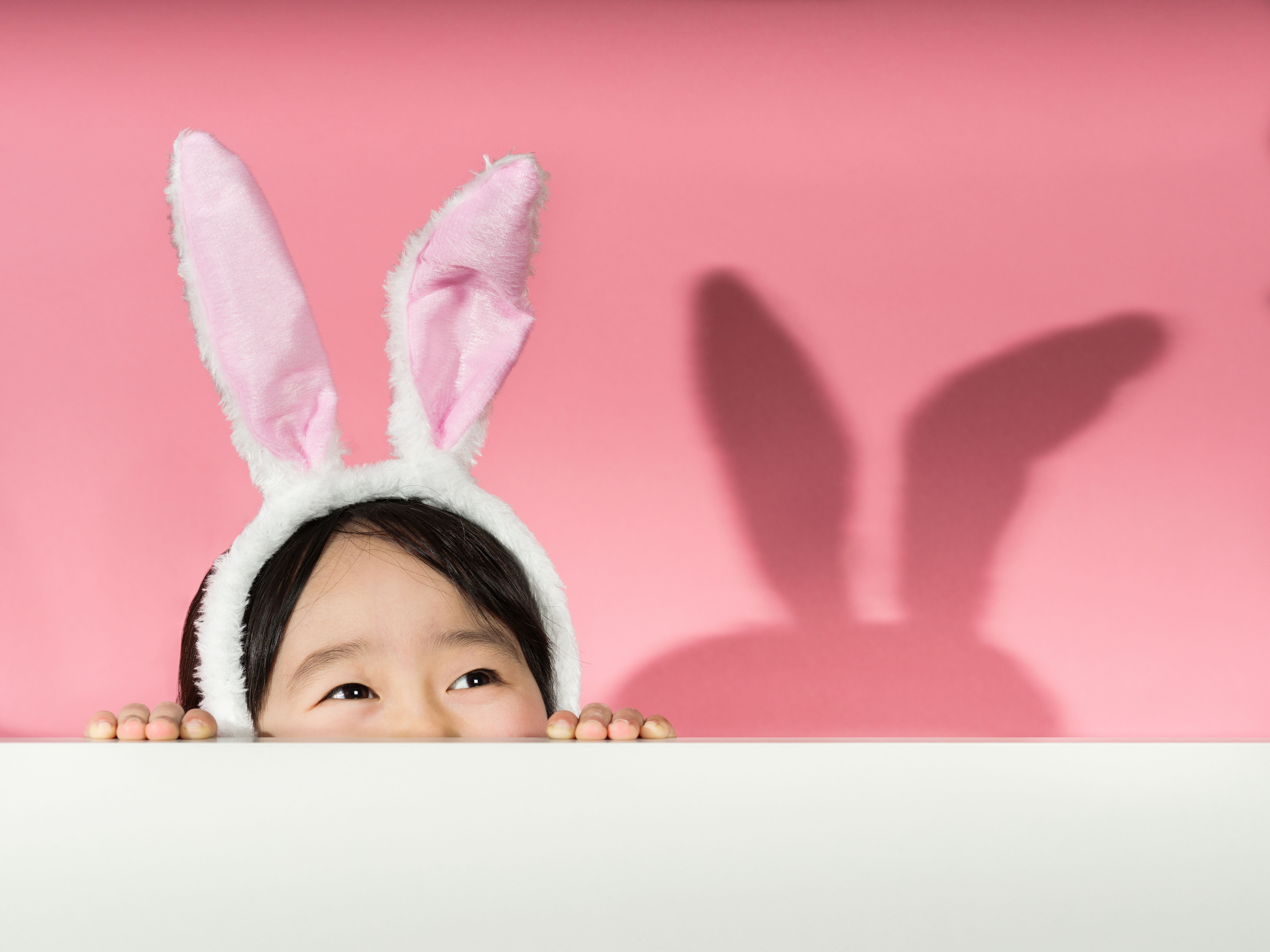 pink background with young girl wearing bunny ears peeking over a white edge 