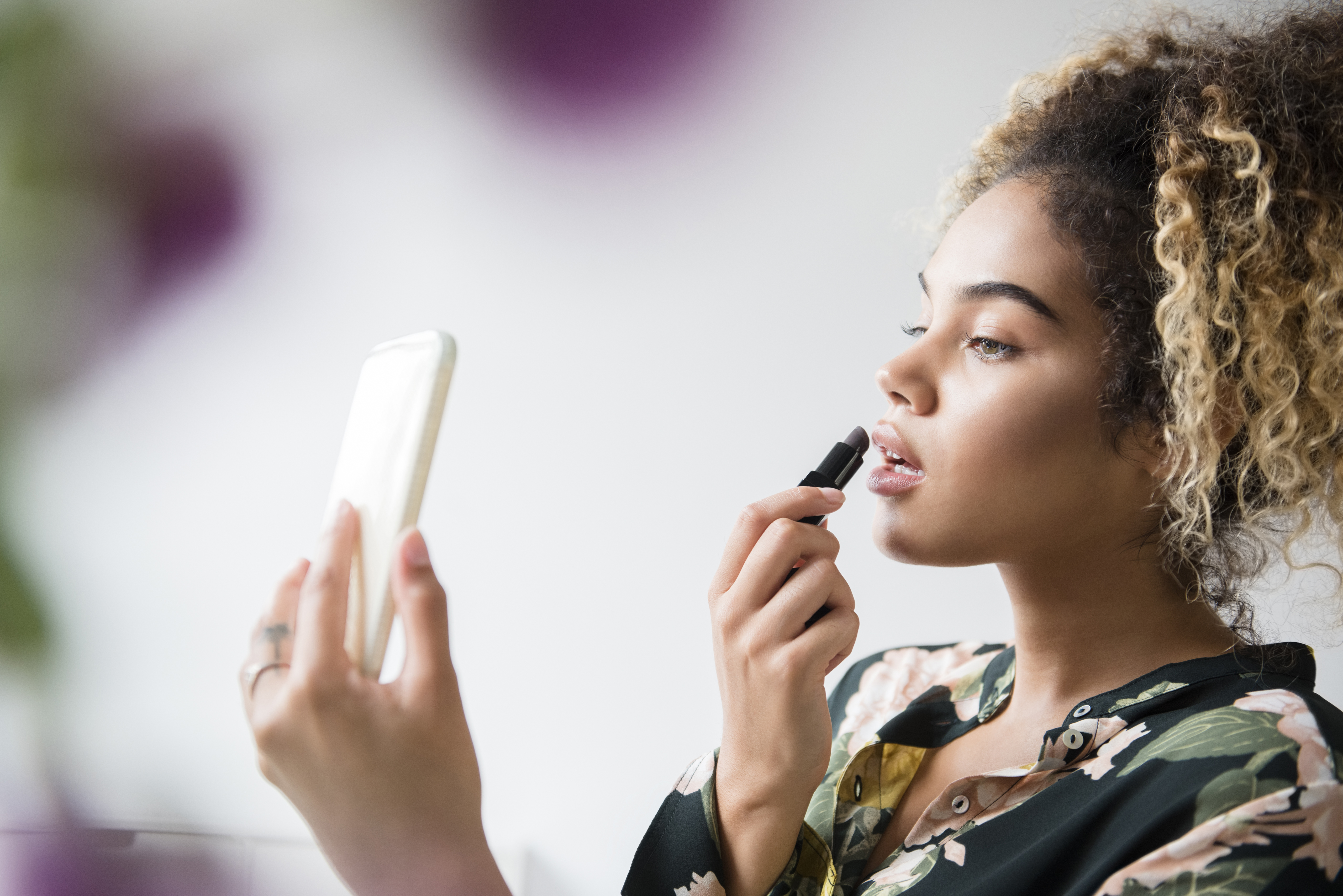 woman looking into compact mirror and applying lipstick