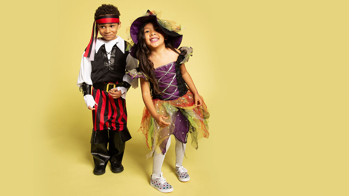 Two Children dressed in a pirate and witch costume with a yellow back drop.