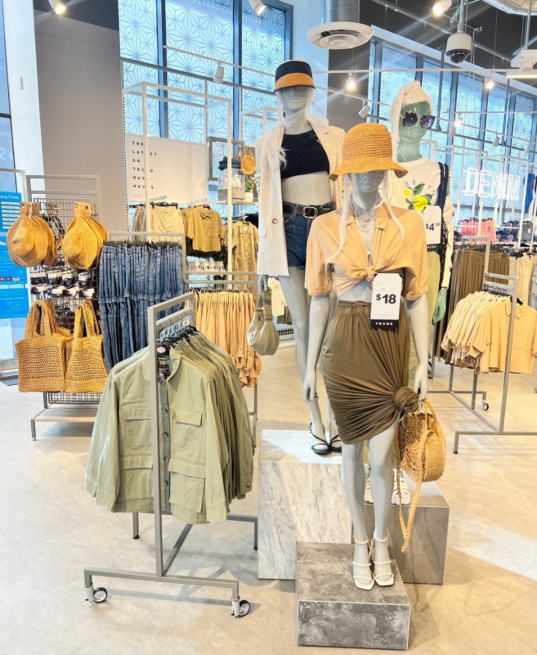 3 mannequins dressed in summer attire. nuetral and green summer attire in store sidplaying bags hats and jackets