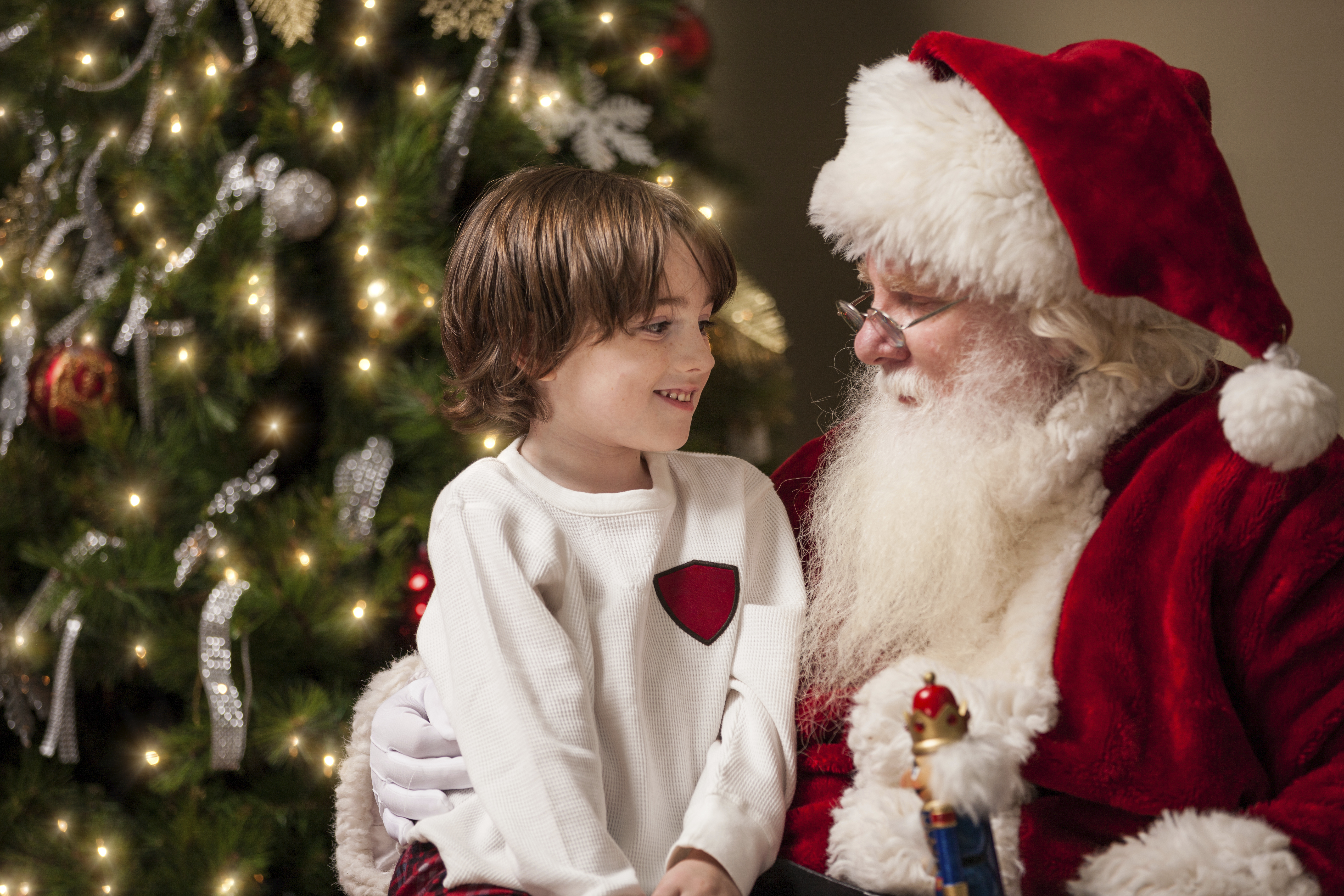 Santa with child on his lap looking at him and Christmas tree in the background